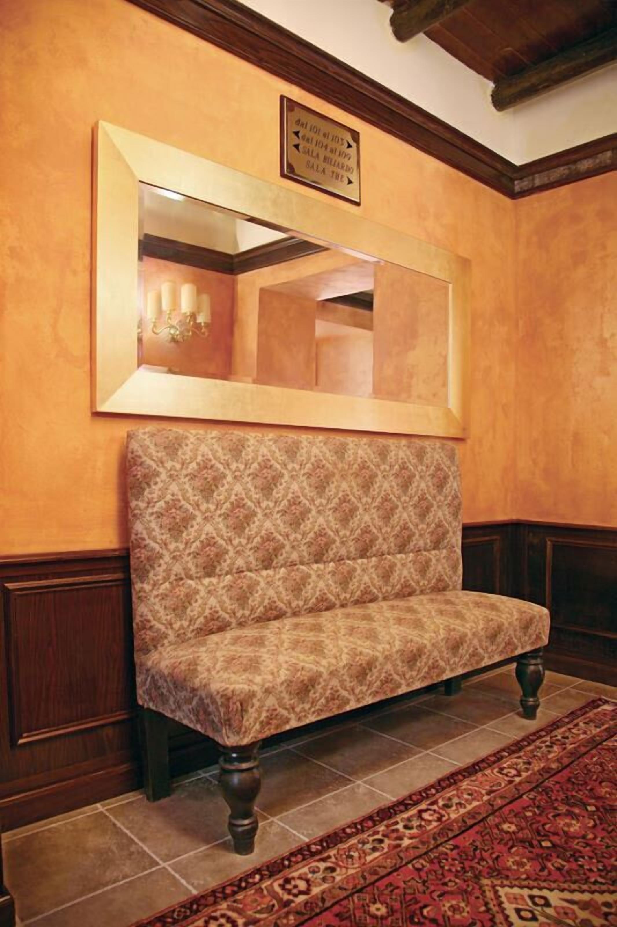 Quarto com um banco estampado, um espelho grande e teto de madeira.