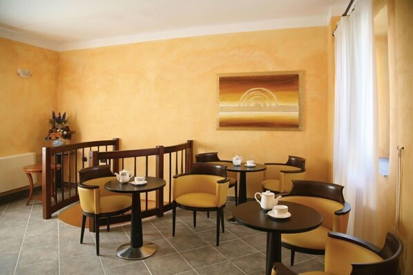 Habitación de hotel con pared amarilla, un cuadro y zona de estar con mesas y sillas.