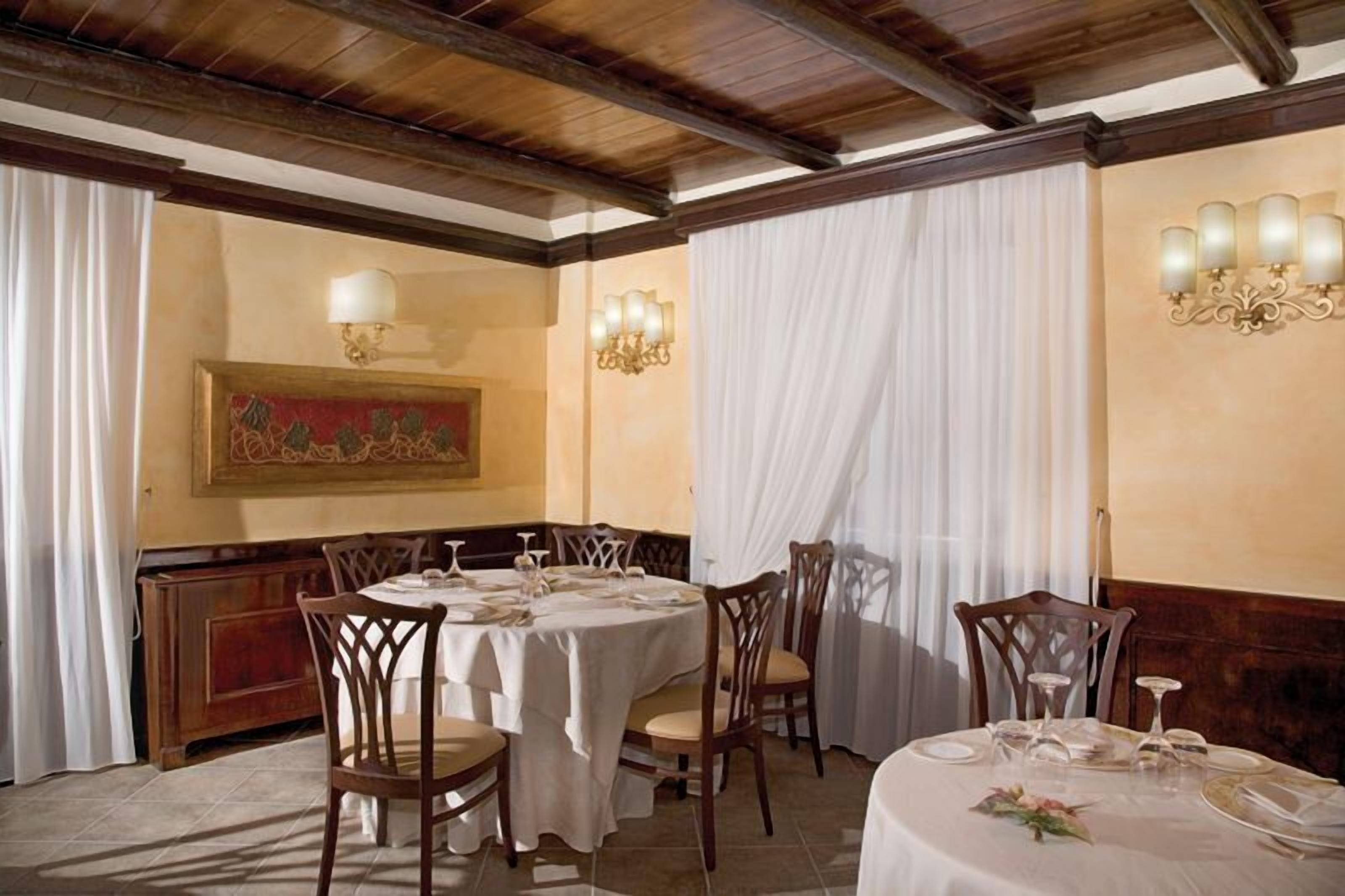A dining area with round tables set for four, wooden chairs, and a chandelier.
