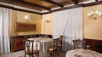 Zona pranzo con tavoli rotondi apparecchiati per quattro, sedie di legno e un lampadario.