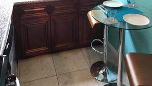 Una cocina con encimera de granito, armarios de madera oscura, pileta de acero inoxidable y mesa de comedor de vidrio.