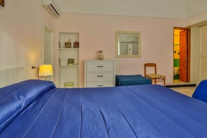 A bedroom with a large bed, a bedside table with a lamp, a dresser, a chair, and a shelf with decorative items. - Heart Of Amalfi (Amalfi)