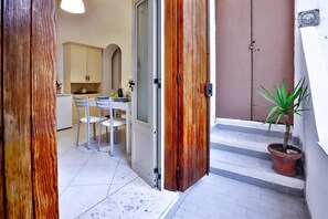 A narrow hallway with a wooden door, a dining area with chairs and a table, and a potted plant on a small staircase. - Heart Of Amalfi (Amalfi)