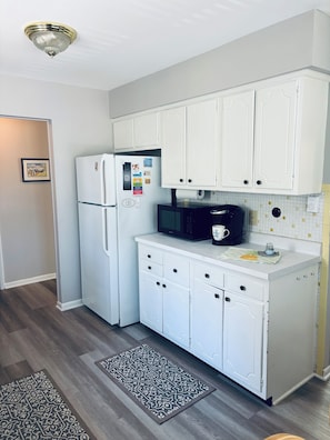 A kitchen with white cabinets, a refrigerator, a microwave, and a patterned rug.