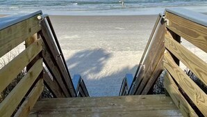 A wooden boardwalk leading to a sandy beach with waves in the background.
