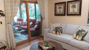 A living room with a sofa, a coffee table with a plant, and a sliding glass door leading to an outdoor seating area.