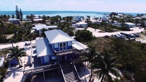 Een pand aan het strand met een opvallend huis, een metalen dak, een balkon en een trap naar de ingang.