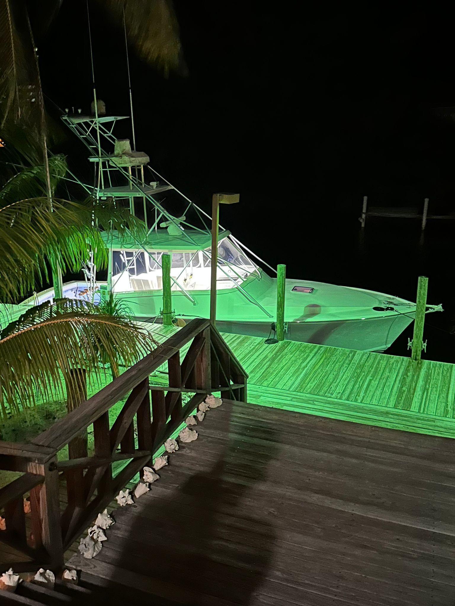A wooden deck with a railing, leading to a green-roofed boat docked at a pier.