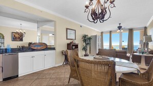 A spacious kitchen with white cabinets, a dining area with wicker chairs, and a large window overlooking the ocean.