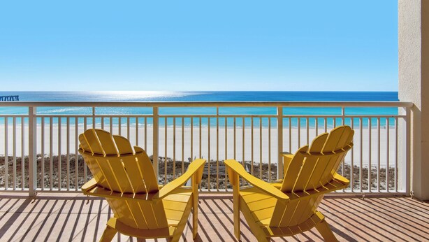 A balcony with two yellow Adirondack chairs facing a beach with a clear view of the ocean.
