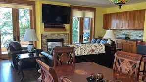 A dining area with a wooden table and chairs, a fireplace, a television, and a kitchen in the background. - Admiral's Suite - Spacious, Flagship Condo as you enter Eastsound (Eastsound)