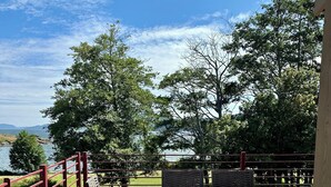 An outdoor patio with a table and chairs, a red railing, and a view of a body of water and trees. - Admiral's Suite - Spacious, Flagship Condo as you enter Eastsound (Eastsound)