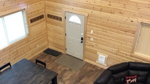 A cozy cabin interior with a wooden interior, a dining table with chairs, a black leather sofa, and a door with a window above it. - #1 Beautiful Cabin In The Heart Of Island Park (Island Park)