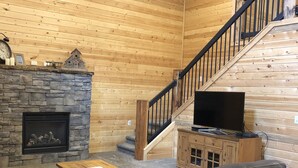 A cozy living room with a stone fireplace, a wooden staircase, a television, and a leather sofa. - #1 Beautiful Cabin In The Heart Of Island Park (Island Park)