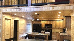 A spacious kitchen with wooden cabinets, a dining area with a large table and chairs, and a balcony with a railing. - #1 Beautiful Cabin In The Heart Of Island Park (Island Park)