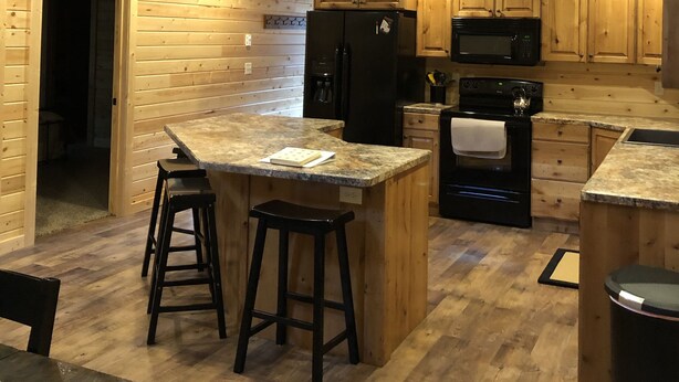 A spacious kitchen with wooden cabinetry, a central island with stools, a microwave, a refrigerator, and a stove. - #1 Beautiful Cabin In The Heart Of Island Park (Island Park)