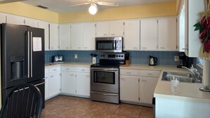 A modern kitchen with white cabinets, a black refrigerator, a microwave, an oven, and a sink.