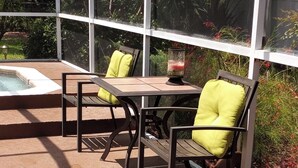 A covered outdoor seating area with a hot tub, chairs, and a table.