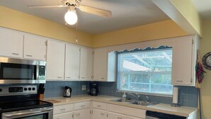 A modern kitchen with white cabinets, stainless steel appliances, a dishwasher, and a window with blinds.