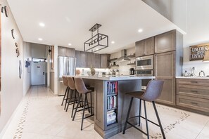 Een moderne keuken met een centraal eiland, barstoelen en een inbouwboekenkast.