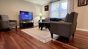 Ein Wohnzimmer mit Flachbildfernseher, einer Couch, einem Couchtisch und einem gemusterten Teppich.