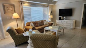 Un salon comprenant un canapé, deux fauteuils, une table basse, un téléviseur et une lampe.