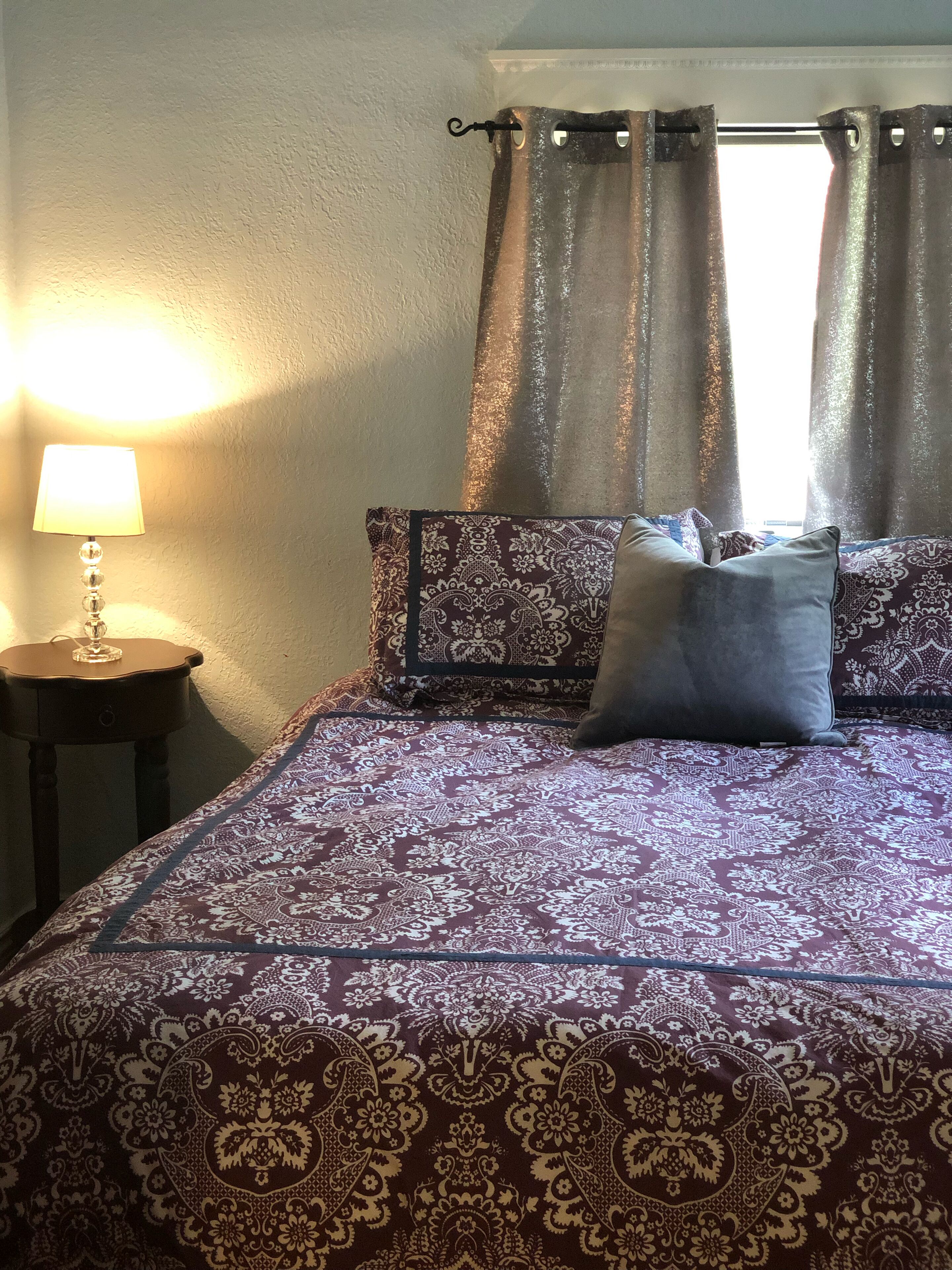 A bed with patterned bedding, a bedside lamp, and curtains.