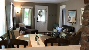 A dining area with a long table, chairs, a sofa, and a door. - Fully Renovated Old Town Cottage Close to Downtown, City Park, and University  (Fort Collins)