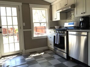 A kitchen with a checkered floor, white cabinets, stainless steel appliances, and a window with a view of a wooden fence.
