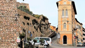 A street with a stone wall, a white van, and a building with a balcony. - Casa Violetta (Portoferraio)