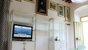 A room with a television on a shelf, wooden beams on the ceiling, and framed pictures on the wall. - Casa Violetta (Portoferraio)