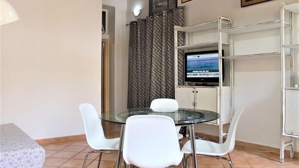 A dining area with a glass table, white chairs, a television on a stand, and a patterned curtain. - Casa Violetta (Portoferraio)