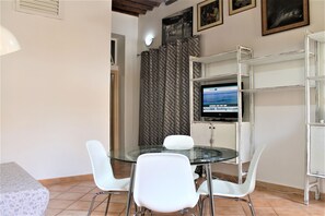 A dining area with a glass table, white chairs, a television on a stand, and a patterned curtain. - Casa Violetta (Portoferraio)