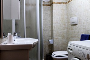A bathroom with a sink, mirror, toilet, and a washing machine.