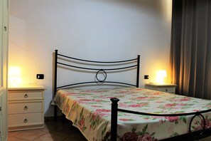 A bed with a floral bedspread, two bedside tables with lamps, and a nightstand with drawers.