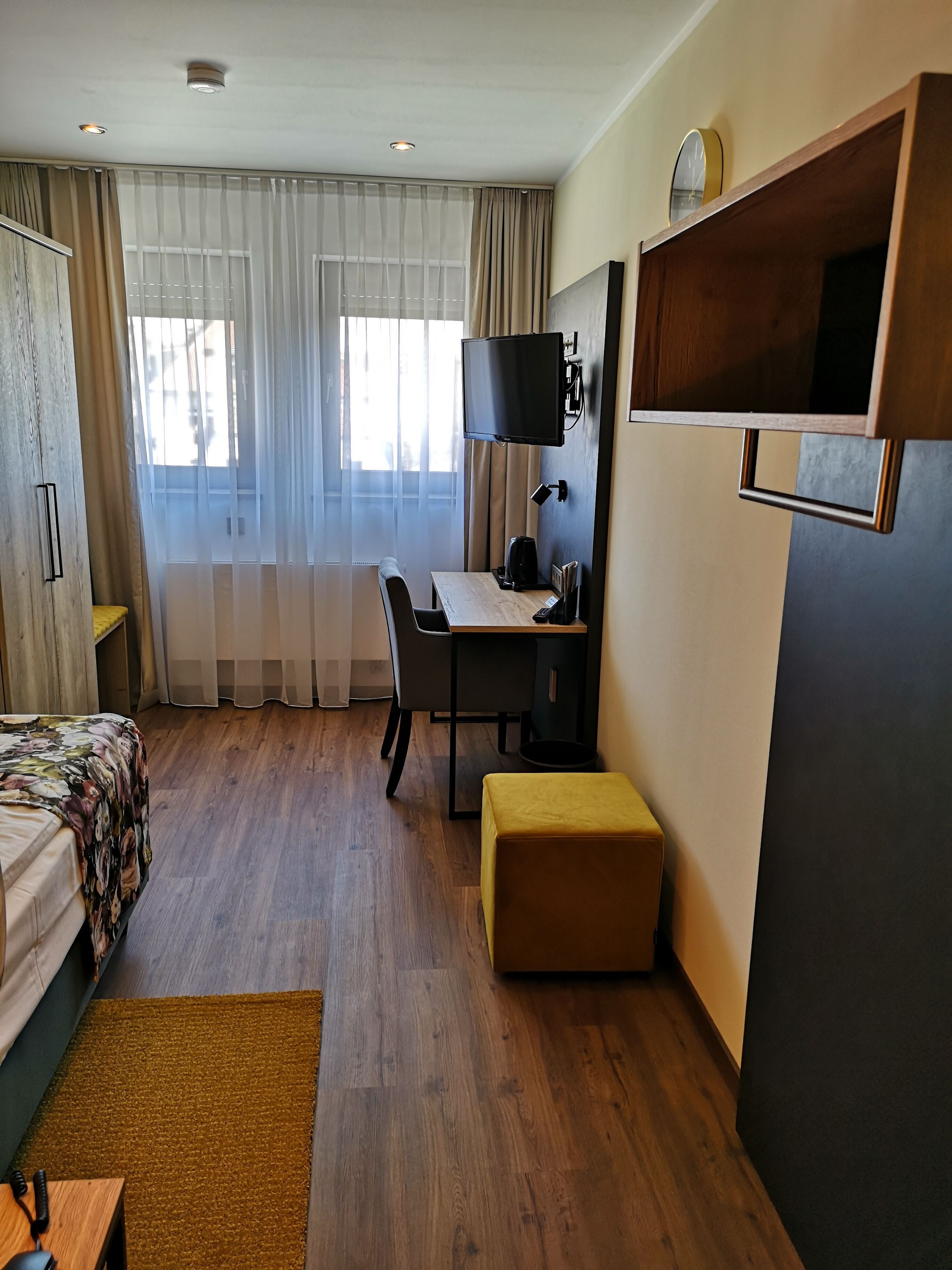 Une chambre d’hôtel moderne avec un bureau en bois, un téléviseur à écran plat fixé au mur, un lit confortable et un petit coin salon.