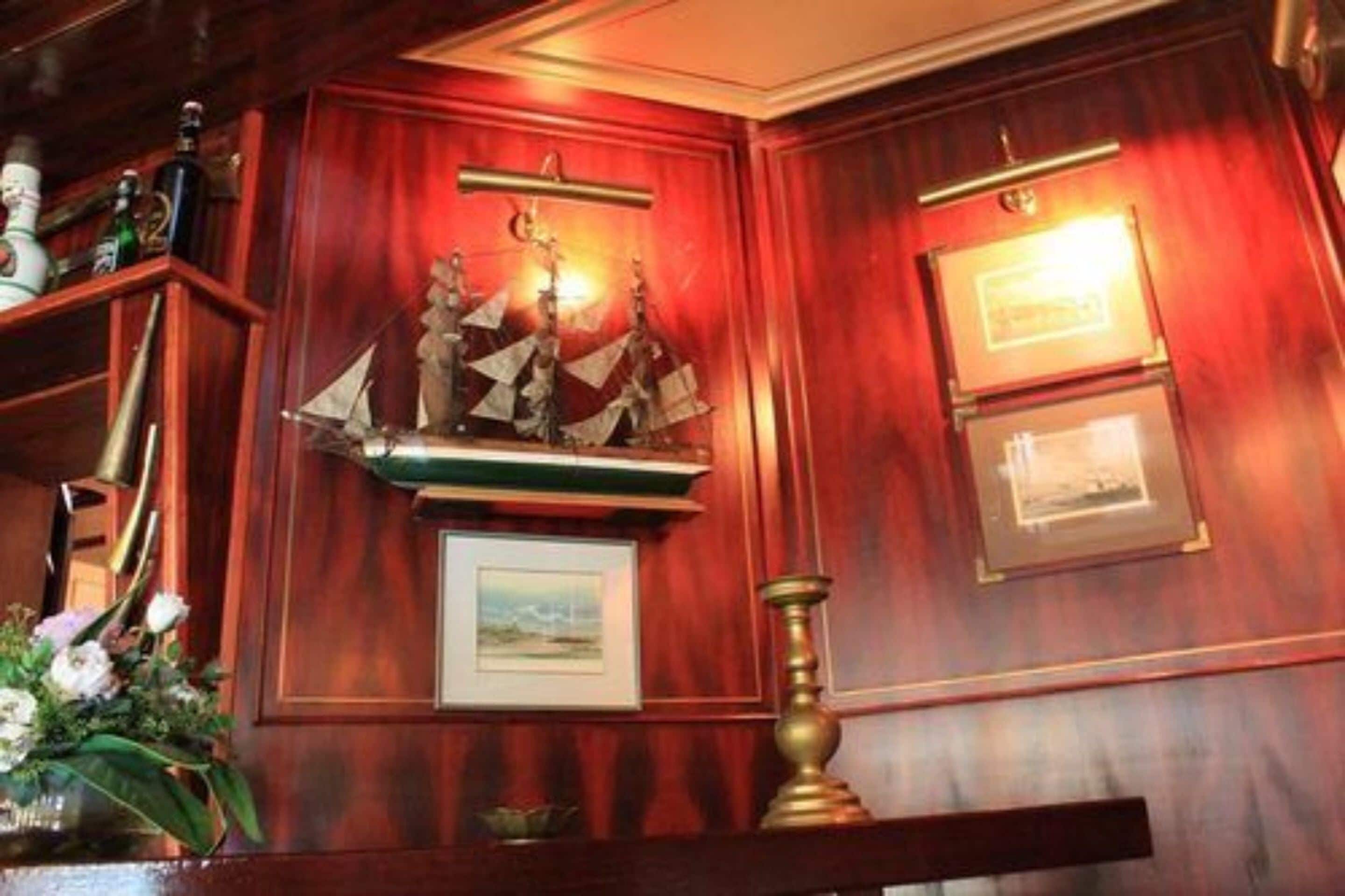 Una pared de madera con obras enmarcadas, un estante decorativo con botellas y un candelabro de latón.