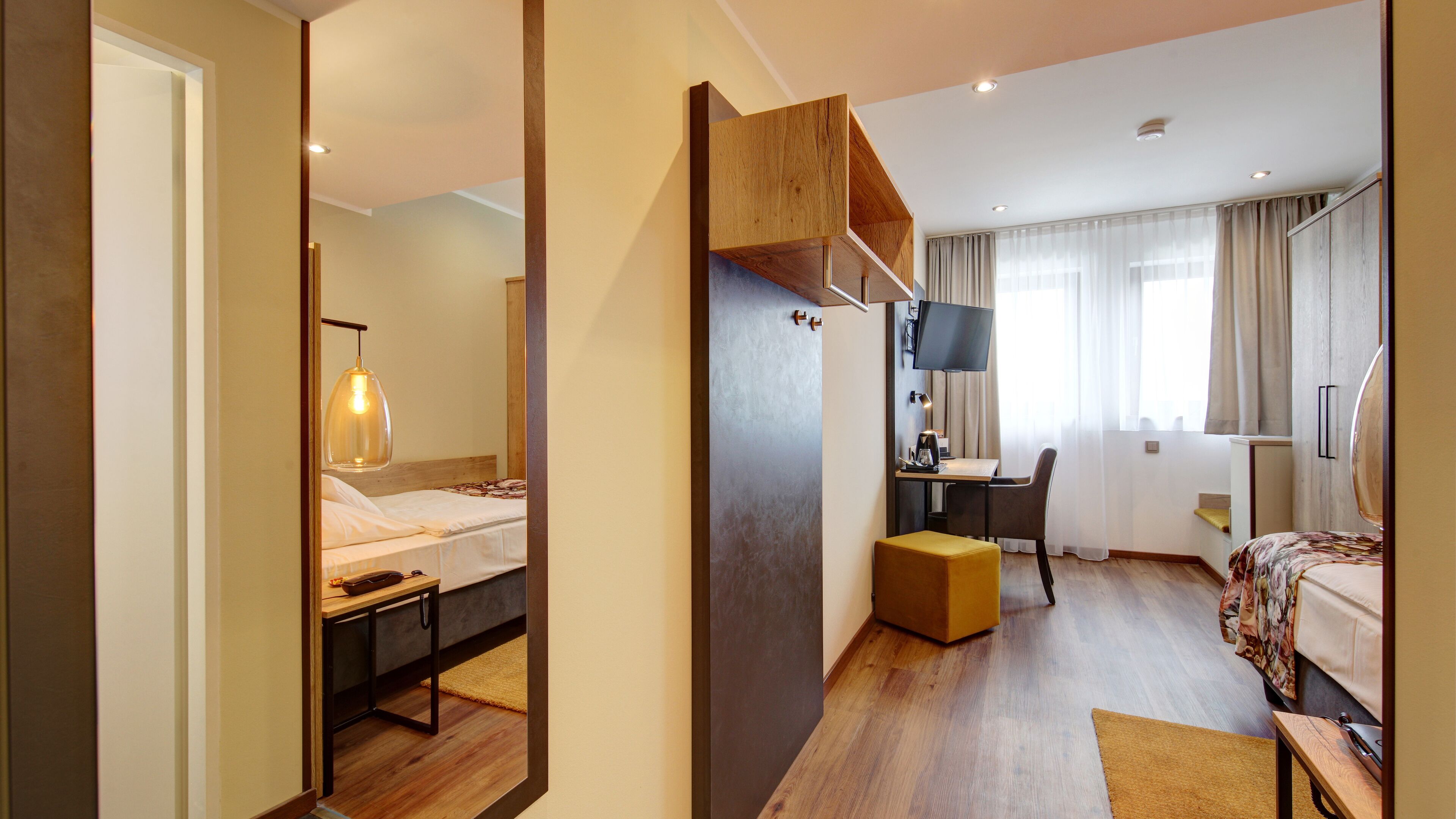 Habitación de hotel con cama, escritorio, silla, televisor y un espejo grande.