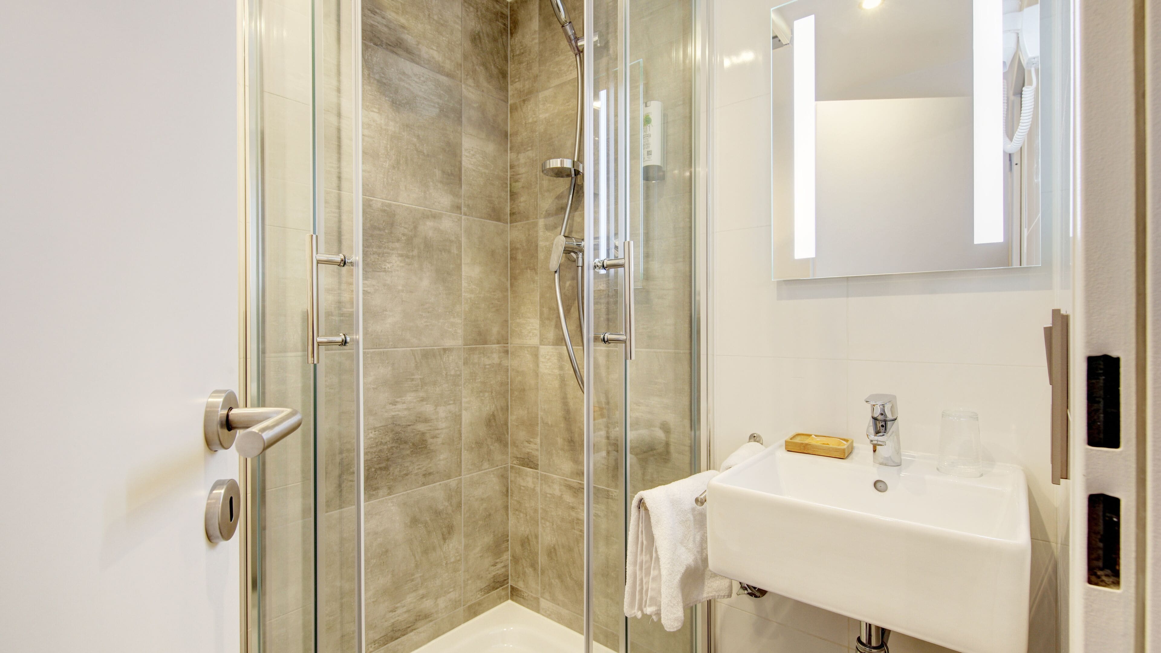Une salle de bain moderne avec une douche à parois de verre, un lavabo blanc et un miroir au-dessus.