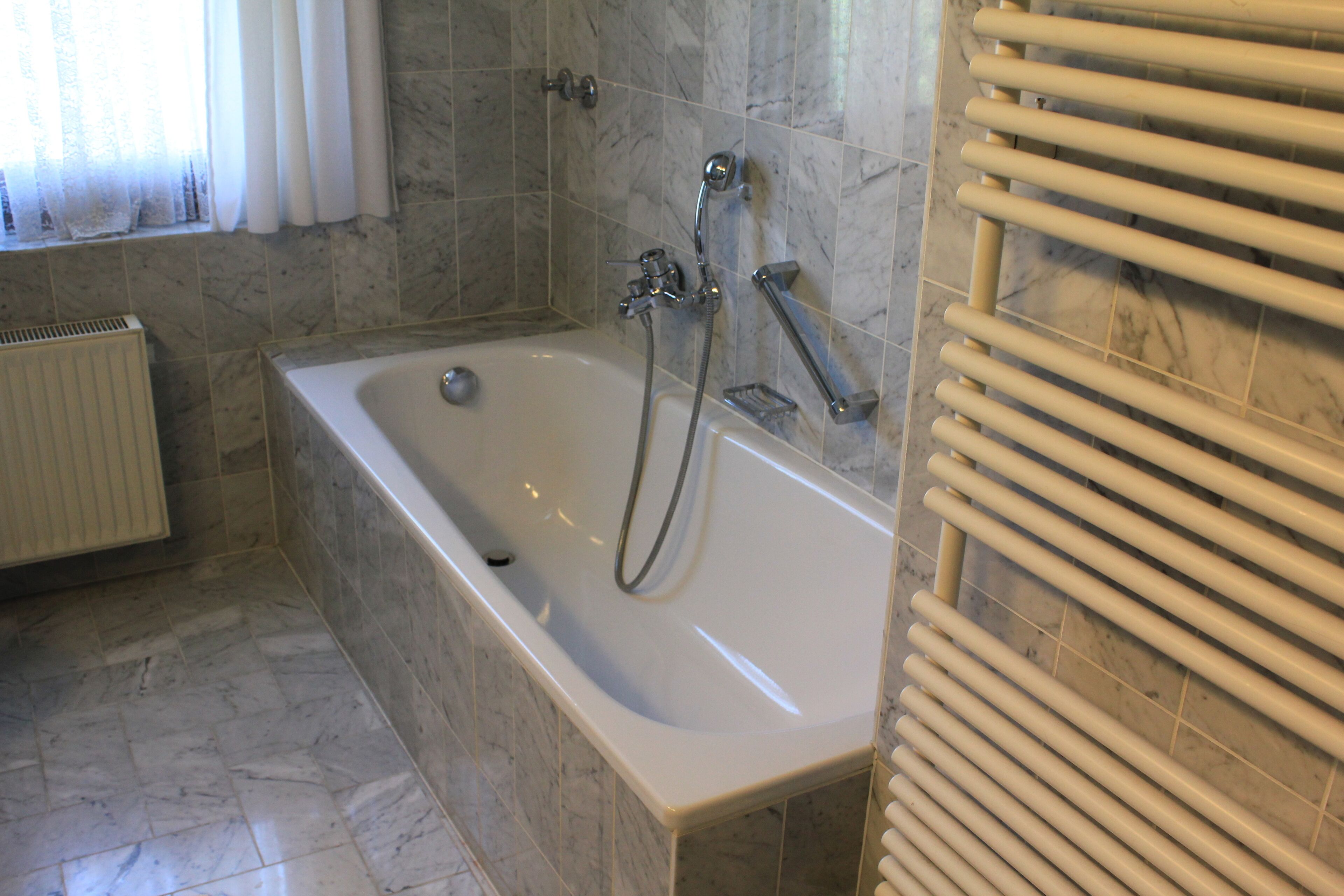 Un bagno moderno con pavimento in marmo, una vasca, una doccia e un porta asciugamani.