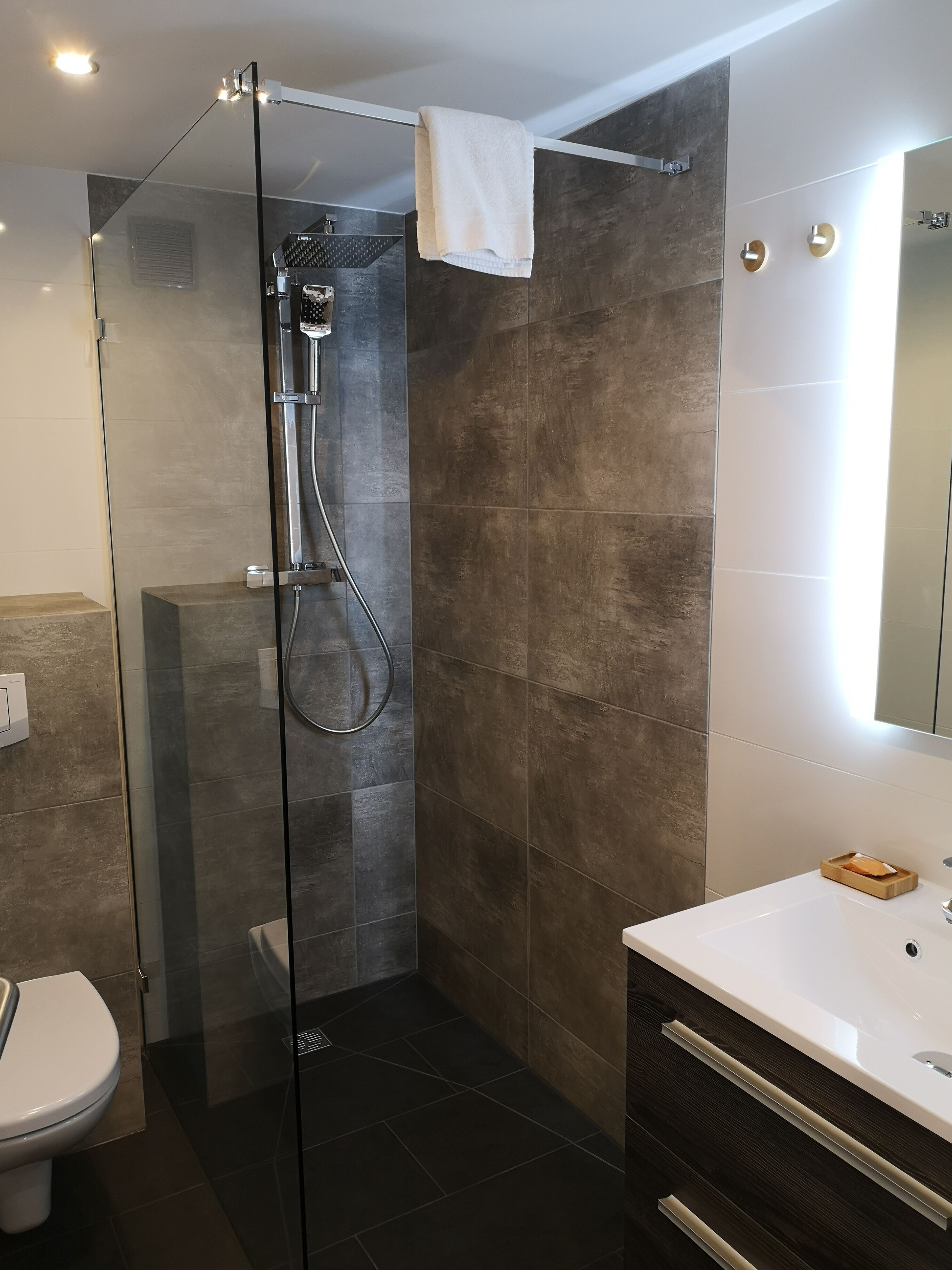 A modern bathroom with a glass-enclosed shower, a white sink, and a mirror with lights.