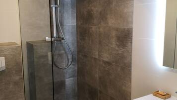 A modern bathroom with a glass-enclosed shower, a white sink, and a mirror with lights.