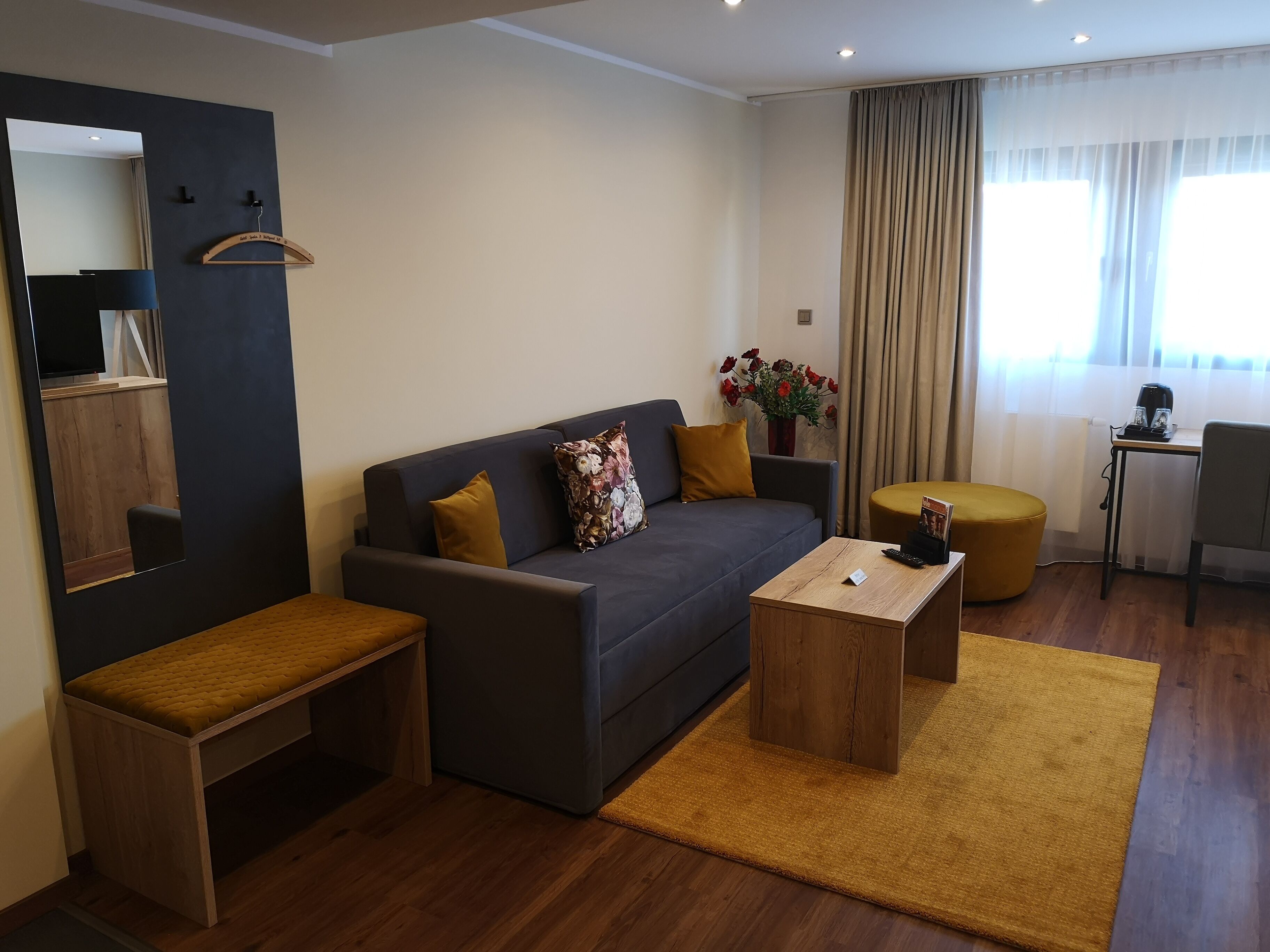 A modern living room with a sofa, a coffee table, a bench, a small table with a kettle, and a chair.