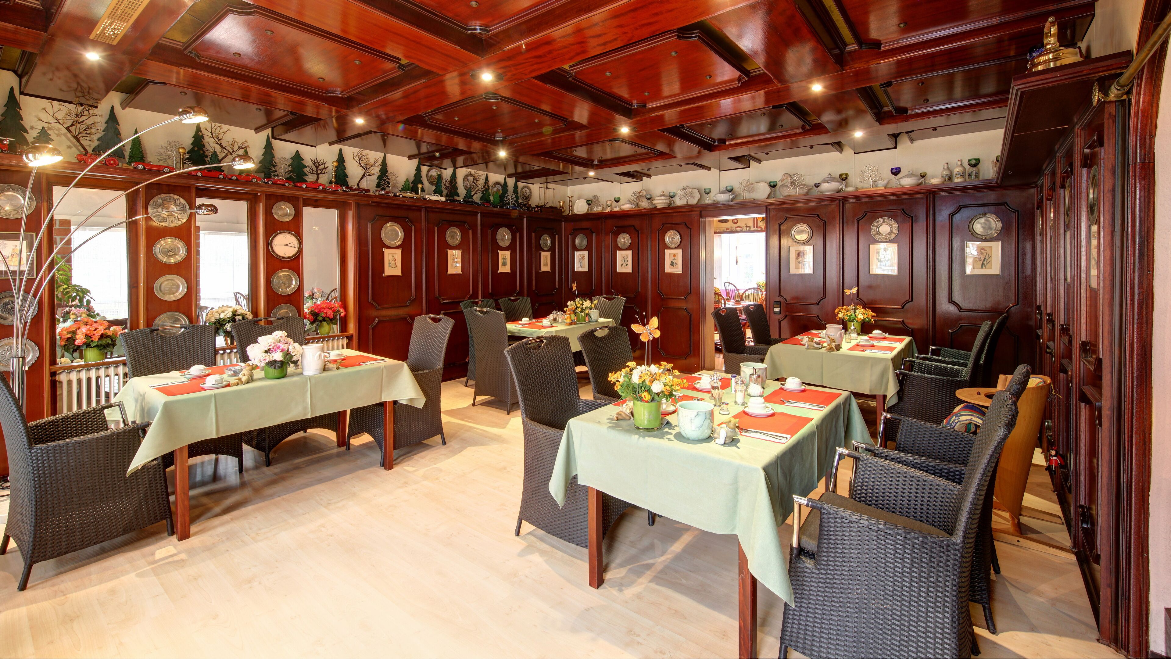 Un comedor con paneles de madera, manteles verdes, sillas de mimbre y centros de mesa florales.