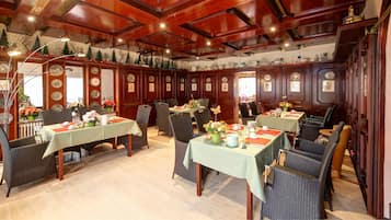 Un comedor con paneles de madera, manteles verdes, sillas de mimbre y centros de mesa florales.