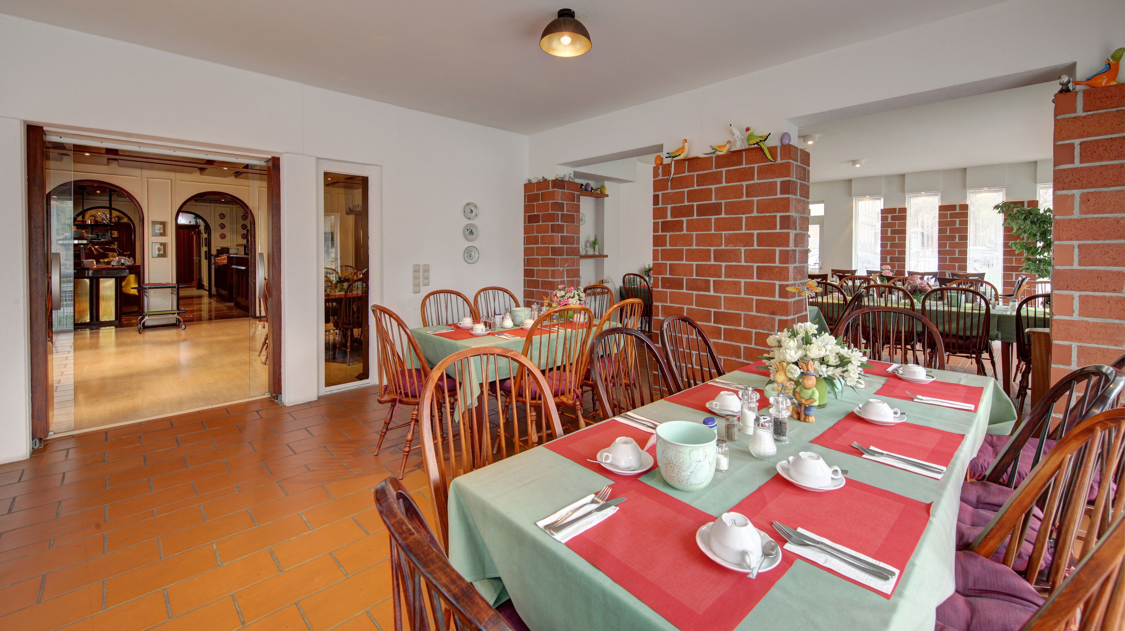 A dining area with brick walls, wooden chairs, and a long table set for a meal.