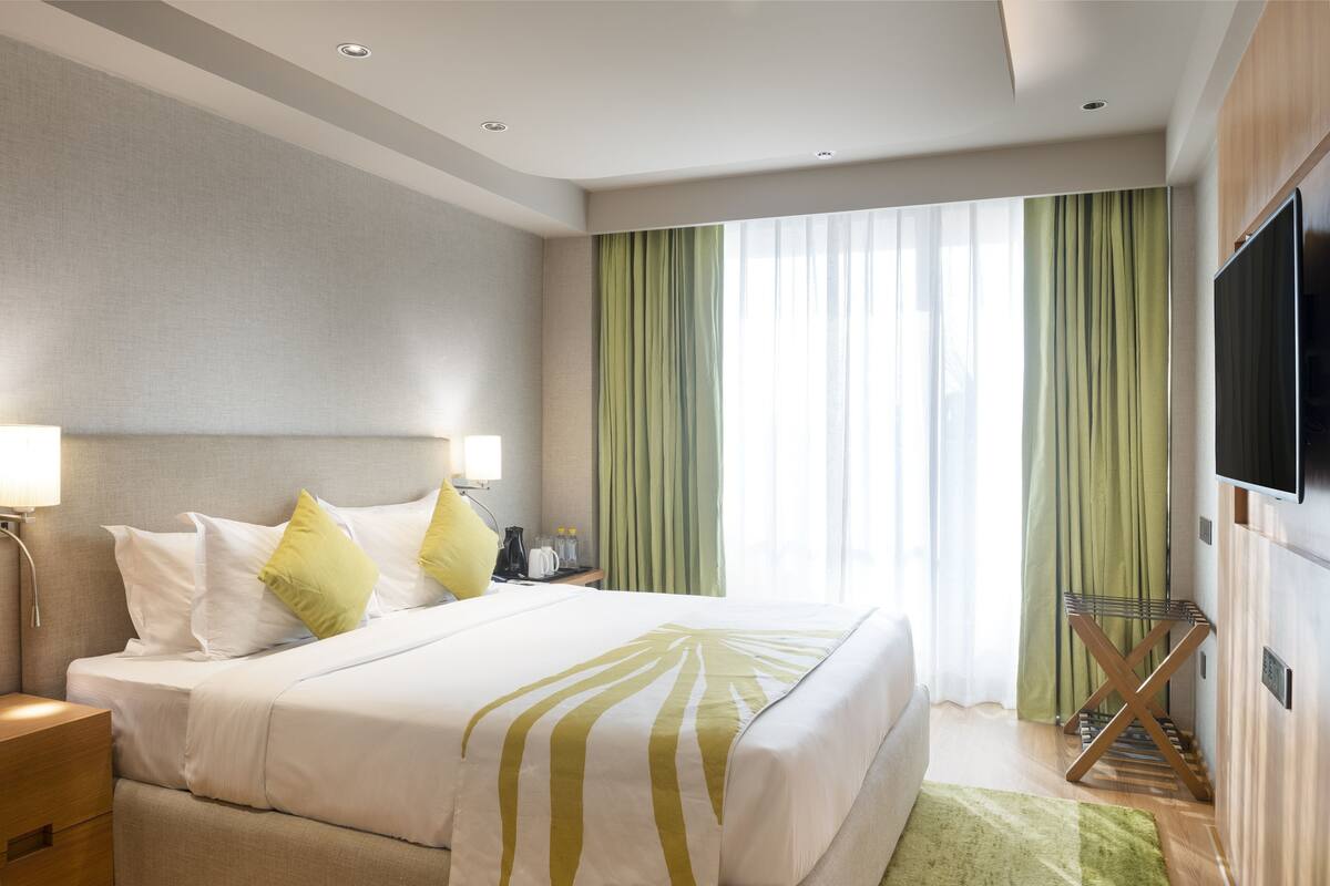 A hotel room with a bed, bedside table, lamp, curtains, and a TV.