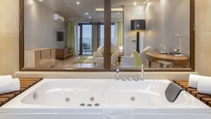 Un baño moderno con una bañera grande, un espejo que refleja una sala de estar con un sofá y una mesa de comedor, y una unidad de aire acondicionado instalada en el techo.