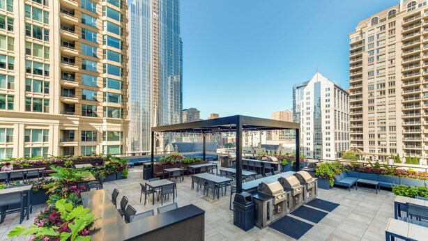 An outdoor patio area with tables, chairs, a barbecue grill, and a covered seating area, surrounded by tall buildings. - LOCATION!!  2b/2b Condo, 51st Floor AMAZING Views, Pool and other Amenities! (Chicago)