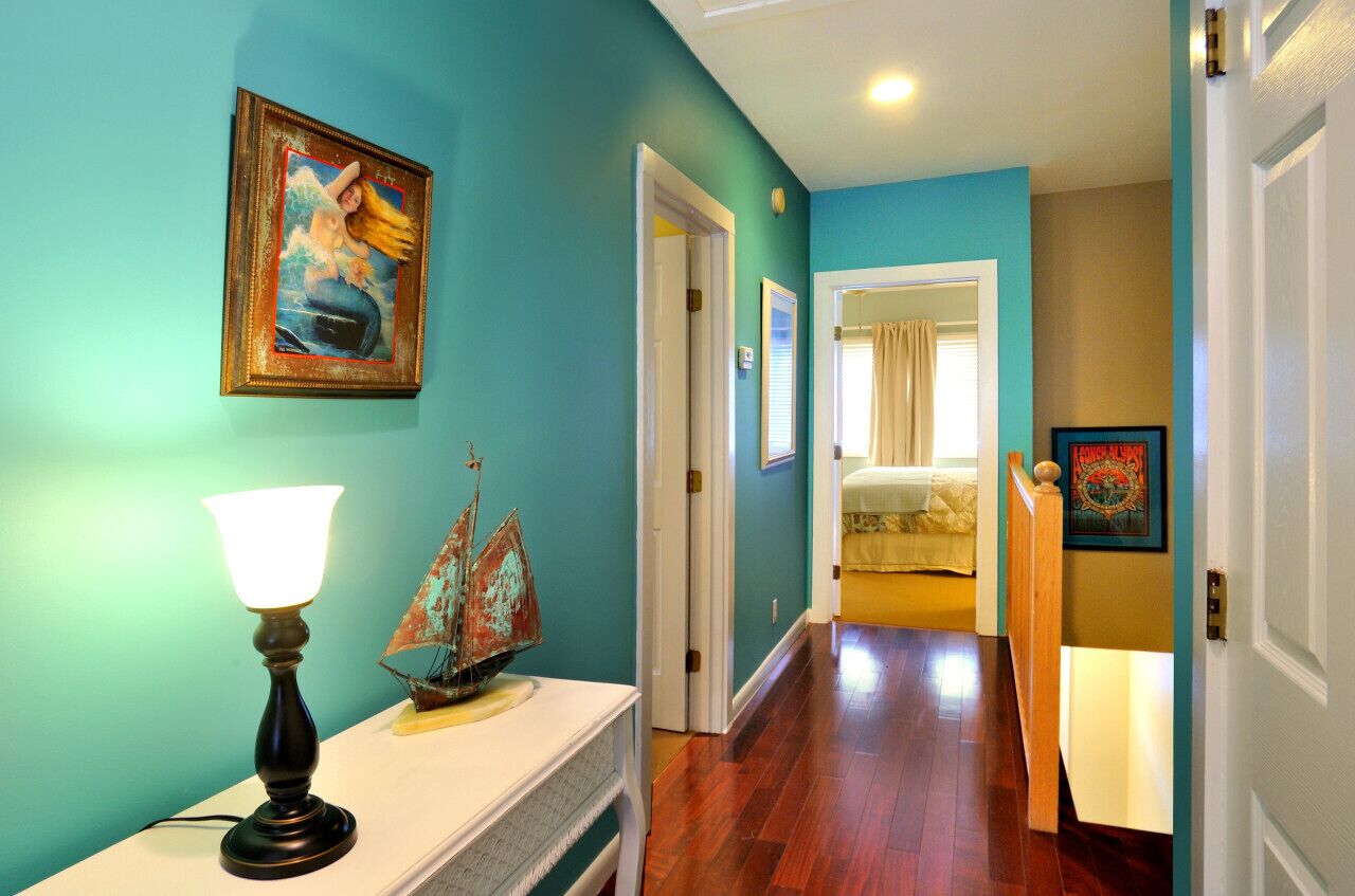 A hallway with teal walls, a wooden floor, a lamp, a framed picture, and a ship model.